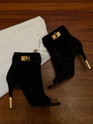 Svarta stövletter från Givenchy - Snygga svarta stövletter från Givenchy i mocka med öppen tå och guldfärgade detaljer på både spänne och klack. Skorna har en elegant siluett och markerade sömmar som ger en exklusiv känsla. Perfekta för dig som vill sticka ut med lyxig design.