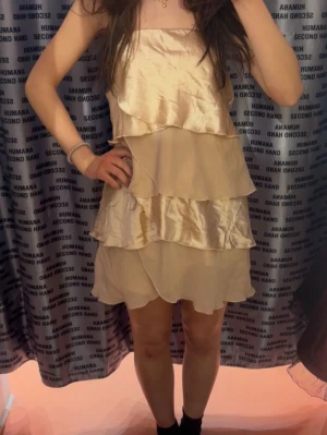  volangklänning - Söt kort klänning i champagnefärgat tyg med flera lager volanger. Jag använde denna på capitol tema fest men går såklart att använda vid vanliga tillfällen också