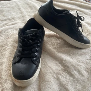 Svarta sneakers med vit sula - Stilrena svarta sneakers med lågt skaft och vita sulor. Skorna har svarta skosnören och metallhål för snörningen. Ovandelen är i slätt material som liknar läder. Passar perfekt till streetwear och casual outfits.