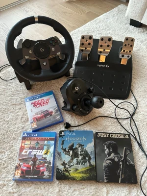 Logitech G920 ratt, pedaler och växelspak - Säljer ett Logitech G920 racing set med ratt, pedaler och växelspak. Ratten är svart med detaljer i metall och har gummiklädd yta för bra grepp. Pedalerna är i metall och plast, och växelspaken är svart. Perfekt för bilspel på Xbox och PC.