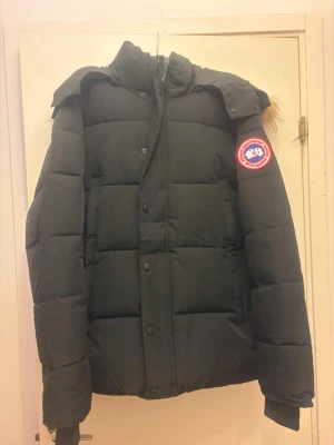 Svart dunjacka från Canada Goose - Säljer en svart dunjacka från Canada Goose med klassisk patch på ärmen. Jackan har en stor huva med  päls. Oanvänd endast testad k 0 p 1 a 