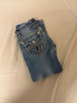 rock revival jeans - Snygga blå jeans från rock revival med unika broderade bakfickor och dekorativa knappar. storlek 31