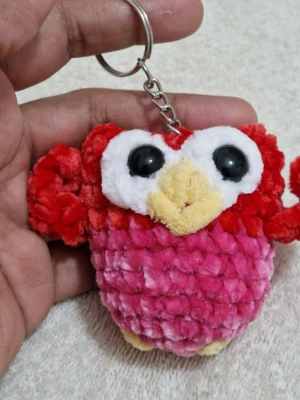 Nyckelring uggla i plysch rosa/röd - Söt nyckelring formad som en uggla i mjuk plysch. Kroppen är rosa och röd med stora vita ögon, svart pupill och gul näbb. Perfekt att hänga på väskan eller nycklarna för en gullig touch.