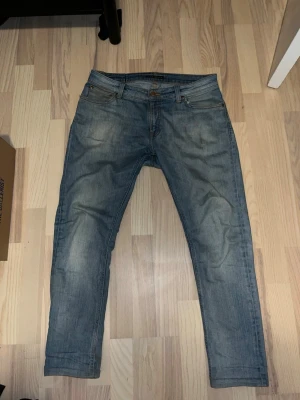 Ljusblå jeans från Nudie Jeans - Säljer ett par ljusblå jeans från Nudie Jeans med klassisk femficksmodell och raka ben. Jeansen har slitningar och diskreta detaljer på bakfickorna. Tillverkade i bomull med en skön passform som funkar till det mesta. En liten skada som är lagad men inget som syns så väl. 