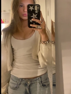 Krämvit kort kofta med ballongärm - Säljer en krämvit kort kofta med ballongärmar och ribbade muddar. Koftan är öppen framtill och har en mjuk, stickad känsla. Perfekt att slänga över ett linne eller t-shirt för en chill look.