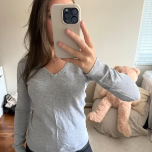 Ljusgrå v-ringad tröja - Snygg ljusgrå långärmad tröja med v-ringning och ribbade muddar. Perfekt att matcha med jeans eller kjol för en clean och enkel look.