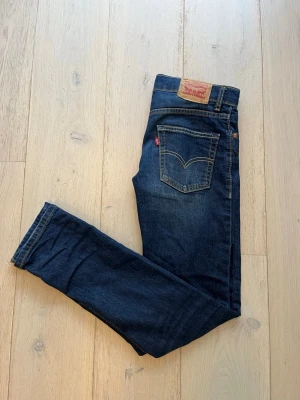 Mörkblå Levi's jeans  - Säljer ett par klassiska mörkblå slim taper jeans från Levi's och femficksmodell. Jeansen har patch i läder bak i midjan. Tillverkade i slitstark denim, perfekta till vardagslooken.