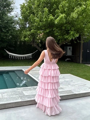 Ljusrosa volangklänning med djup rygg - Super fin klänning, perfekt till bal eller någon finare middag. Endast använd ett tillfälle, sparsamt. Insydd ovanför midjan och banden, men går att sprätta upp. Hör av dig vid intresse, vid snabbt köp kan  pris diskuteras. 