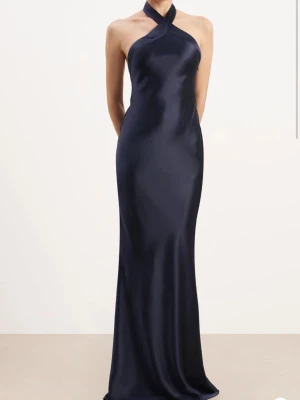 Balklänning marinblå - Helt ny aldrig använd marinblå balklänning i satin storlek M. Köpt i London. Halterneck med en fin hög skurning fram samt låg rygg som ger en exklusiv känsla. Lapparna finns kvar. Perfekt för dig som vill ha en unik och exklusiv balklänning till studenten. Jag är 183cm och den når hela vägen till marken🥰