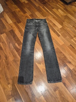 Gråa  Nudie Jeans - Säljer ett par svarta/gråa jeans från Nudie Jeans med snyggt slitna detaljer och kontrastsömmar på bakfickorna. Klassisk rak passform och normal midja. Jeansen har en cool tvättad look och är tillverkade i slitstarkt bomullsmaterial.