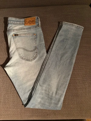 Ljusblå skinny jeans från Lee - Snygga ljusblå skinny jeans från Lee med klassisk femficksdesign och läderpatch bak i midjan. Jeansen har en tvättad look med slitningar framtill och smal passform som sitter tight längs benen. Perfekta till en avslappnad streetstyle.