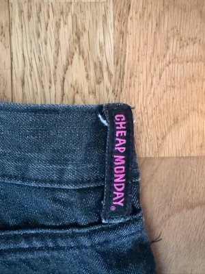 Svarta raka jeans Cheap Monday - Säljer ett par svarta jeans från Cheap Monday med raka ben. Jeansen har en diskret tvättad look och etikett med rosa text i linningen. Perfekta för en avslappnad stil. 