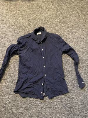 Mörkblå slim fit skjorta från Eton - Snygg mörkblå skjorta från Eton i slim fit-modell. Skjortan har diskret mönster, klassisk krage och vita knappar framtill. Tillverkad i mjuk bomull som känns skön mot huden. Perfekt för dig som gillar stilrena detaljer och en modern passform.