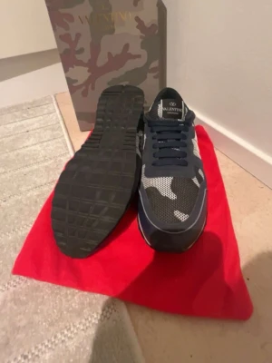 Valentino rockrunners  - Snygga sneakers från Valentino med svart, vit och grå camomönstrad ovandel i mesh och mocka. Skorna har svarta snören, vit sula och cool kontrast mellan material. Perfekta för dig som vill sticka ut med exklusiva detaljer och streetwear-vibe. Allt på bilden skickas med om du har fler frågor e det ba o skriva