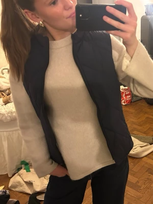 Mörkblå dunväst med ståkrage - Snygg mörkblå dunväst med ståkrage och diskret quiltat mönster. Västen är lätt och perfekt att slänga över en tröja för extra värme. Enkel och stilren design som passar till det mesta. Perfekt för lager-på-lager-stil.