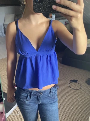 Blå v ringad topp - Säljer en kornblå linnetopp med smala axelband och v-ringning. Toppen har en luftig, lätt utsvängd passform och är croppad i modellen. Dragkedjan är lite trasig vid sidan 