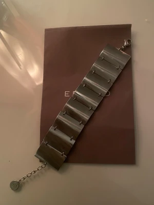 Brett silverfärgat armband från Edblad - Stilrent och brett armband i silverfärgad metall från Edblad. Armbandet består av flera rektangulära länkar och har en justerbar kedja med en rund Edblad-logga vid låset. Perfekt för dig som gillar statement-smycken. Armbandet ligger på runt 500-600 nypris. Skickas i en orginal Edblad påse.
