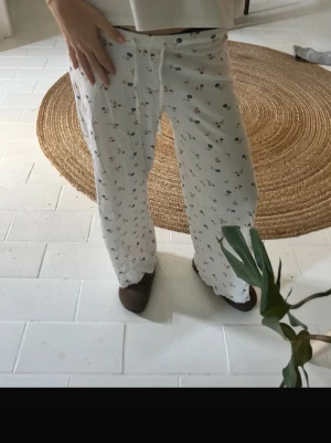Vita pyjamasbyxor med småmönster - Mysiga vita pyjamasbyxor med små blommiga och färgglada detaljer. Byxorna har rak passform, resår i midjan och dragsko för extra komfort. Perfekta för slappa dagar hemma eller när du vill chilla i soffan.