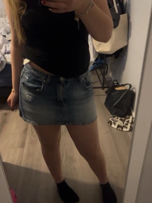 Blå jeanskjol med slitningar - Säljer en blå jeanskjol i kort modell med slitna detaljer och klassiska fickor fram och bak. Kjolen har en knapp och dragkedja framtill och är perfekt för en avslappnad stil. Passar till det mesta och är enkel att matcha. Nypris är 329kr och är använd max 3 gånger så inga skambud.