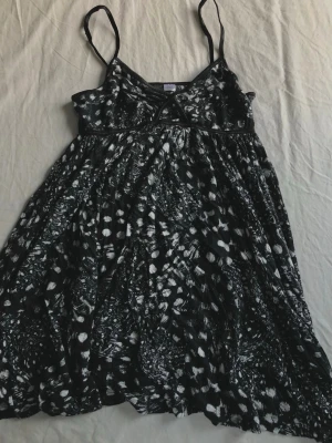 Svartvit kortklänning med mönster - Svartvit stretchig kortklänning med smala axelband och ett unikt abstrakt mönster. Klänningen har en lätt utställd passform och markerad byst med dekorativ söm. Perfekt till sommaren.