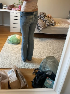 Blå bootcut jeans med slitningar - Säljer ett par blå bootcut jeans med slitningar på knäet och klassiska bakfickor. Jeansen har en något utsvängd passform nertill och är i denim med ljusa tvättade detaljer. Perfekta för en avslappnad och trendig look.