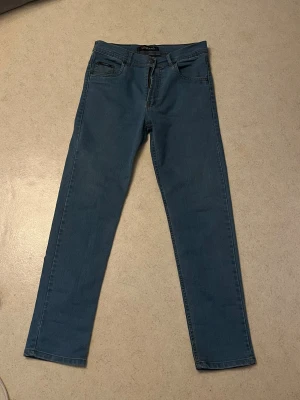 Blå raka jeans från Wrangler - Snygga blå jeans från Wrangler med rak passform och klassisk femficksdesign. Jeansen har bälteshällor, dragkedjegylf och detaljerade sömmar. Perfekta för en avslappnad och stilren look. Materialet är denim i bomull.