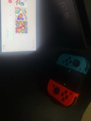 Nintendo Switch med 3 spel som ingår med över värde på 1000kr - Nintendo Switch spelkonsol med röda och blå Joy-Con-kontroller. Som har 3 spel som är över 1000kr sammanlagt. Konsolen har en svart rektangulär form och medföljande dockningsstation. Perfekt för gaming både hemma och på språng. Skärmen är i färg och kontrollerna är av plast. 
