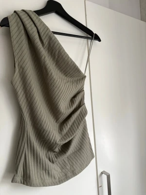 Ribbad oneshoulder topp från Zara - Trendig ribbad topp från Zara i en snygg grön färg. Modellen är oneshoulder.