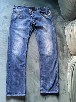 Replay blå jeans med knappar - Design med raka ben och knäppning med flera knappar framtill. Jeansen har klassiska fickor och slitningar som ger en cool, använd look. Perfekt för dig som gillar en avslappnad stil. Tvättas i 30 grader. 98 % bomull 2 % elastan W 33 Längd 34