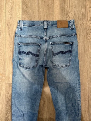 Nudie Jeans Thin Finn Blå W29/L32 - Slim Fit - Mycket fint skick. Mått - Midja: 35cm, Ytterbenslängd: 101cm, Benöppning: 15,5cm. Modellen är 185cm & 63kg. Hör av dig vid funderingar!🤝