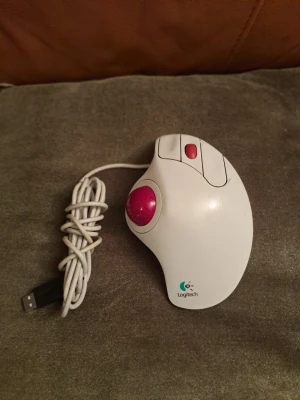 Logitech TrackMan Marble Wheel (T-BB13) – Klassisk Trackball med USB - Säljer en legendarisk Logitech TrackMan Marble Wheel i det eftertraktade vita utförandet med röd kula. Detta är modellen T-BB13 som har inbyggt scrollhjul och smidig USB-anslutning, vilket gör att den fungerar direkt med moderna datorer utan adaptrar. Perfekt för dig som söker en ergonomisk mus som minskar belastningen på handleden, eller för dig som vill ha reservdelar till din favoritmodell som inte längre tillverkas. Detaljer: Modell: T-BB13, Anslutning: USB, Funktioner: Optisk avläsning. 