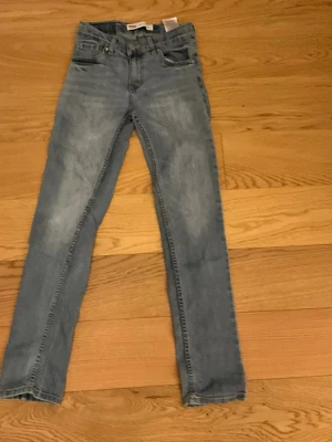 Ljusblå skinny jeans från Levi's - Säljer ett par ljusblå jeans från Levi's med klassisk femficksdesign och raka ben. Jeansen har en snygg tvättad look och är tillverkade i bomull. Perfekta för en avslappnad och trendig stil. Storlek 158.