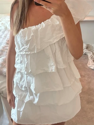 Vit volangklänning - Säljer en superfin vit klänning med volanger och oneshoulder. Står ingen storlek i den men gissar att det är M i TALL. För referens är jag 178 och brukar ha M. Sitter bra på mig men är resår så skulle säga att den passar även S eller L! Den är från Anielle och nypris är 1395kr. Använd en gång men är som ny🌻 