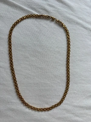 Mockberg Guldfärgat kedjehalsband - Stilrent halsband i guldfärgad metall med tvinnad kedja. Halsbandet har en klassisk design med rundade länkar som ger ett elegant intryck. Perfekt för att lyfta vilken outfit som helst med en touch av guld. Ifrån mockberg 