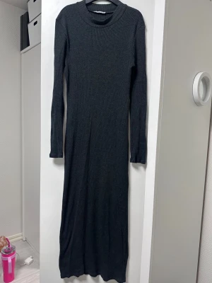 Mörkgrå ribbad långklänning - Säljer en stilren mörkgrå långklänning i ribbad bomull. Klänningen har lång ärm, rund halsringning och en figurnära passform som ger en clean look. Perfekt för dig som gillar minimalistisk stil och vill ha något bekvämt men ändå snyggt. Storlek L men känns som ett M