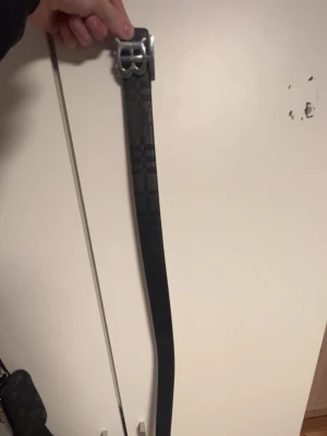 Vändbart bälte med rutig och svart sida - Säljer ett vändbart bälte med en sida i klassiskt beige-rutigt mönster och en sida i svart. Bältet har ett stort, silverfärgat spänne och är perfekt för dig som vill kunna variera din stil. Passar till jeans eller byxor för en trendig look.