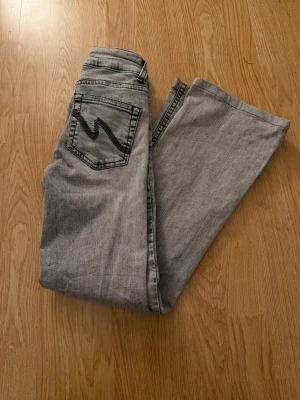 Grå bootcut jeans från Nelly - Säljer ett par grå bootcut jeans från Nelly med låg midja. Jeansen har en snygg svart broderad detalj på bakfickan och klassisk femficksdesign. Perfekta för dig som gillar en avslappnad men trendig look.