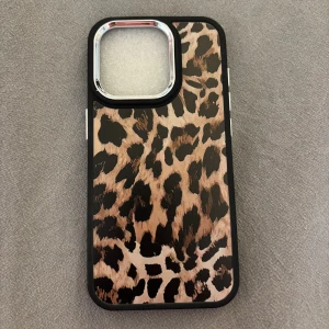 Leopardmönstrat mobilskal iPhone 15 PRO - Snyggt mobilskal med leopardmönster i beige, brunt och svart. Skalet har en svart ram och silvriga detaljer runt kameran. Tillverkat i tålig plast som skyddar mobilen och ger ett trendigt intryck. Perfekt för dig som vill sticka ut med din mobil!