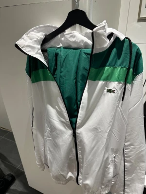 Grön och vit tracksuit från Lacoste - Säljer en snygg tracksuit från Lacoste i grönt och vitt. Jackan har dragkedja, huva och Lacoste-logga på bröstet. Passar dig som är 180+, byxorna är lite mindre i storlek. Perfekt för dig som vill gå med stil. materialet är glansigt och lätt. Skriv över det minsta lilla eller över den minsta funderingen!🔥🔥