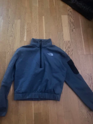 Grå half-zip hoodie från The North Face - Snygg grå fleece hoodie från The North Face med half-zip framtill och hög krage. Loggan är tryckt i vitt på bröstet och det finns en svart ficka på ena ärmen. Aldrig använd så är i väldigt bra skick!