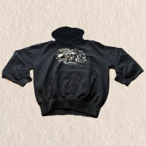 Svart My Chemical Romance hoodie - Svart hoodie med vit grafisk print av My Chemical Romance på bröstet. Klassisk känguruficka framtill, huva med dragsko och ribbade muddar. Perfekt för dig som gillar alternativ stil och bandmerch.