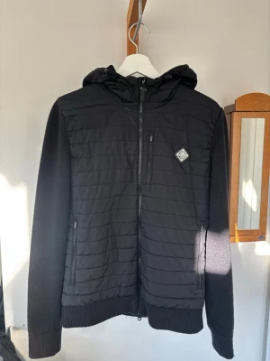 Svart J.Lindeberg cardigan - Svart cardigan med quiltad front och rygg, stickade ärmar och huva. Den är i mycket fint skick och väldigt skonsamt använd, inga defekter! Kan skickas! 