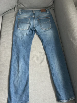 Blå jeans från Nudie Jeans - Säljer ett par klassiska blå jeans från Nudie Jeans med raka ben. Jeansen har två bakfickor med den ikoniska Nudie-sömmen och patch i läder bak i midjan. Tillverkade i mjuk denim som sitter skönt hela dagen. Modell thin finn