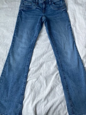Blå bootcut jeans med mellanblå tvätt - Säljer ett par klassiska blå bootcut jeans i mellanblå tvätt. Jeansen har fem fickor, normal midja och lätt utsvängda ben. Perfekta till sneakers eller boots och tillverkade i mjuk denim med lite stretch för extra komfort.