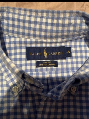 Blårutig skjorta från Ralph Lauren - Snygg blårutig skjorta från Ralph Lauren i modellen Slim Fit Stretch Oxford. Skjortan har klassisk krage, långa ärmar och knäppning framtill. Tillverkad i ett stretchigt material som ger extra komfort och passform.