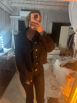 Svart jeansjacka  - Cool svart jeansjacka med klassisk krage och silverfärgade knappar framtill. Jackan är kortare i modellen och har långa ärmar. Perfekt att slänga över en t-shirt eller hoodie för en avslappnad look.