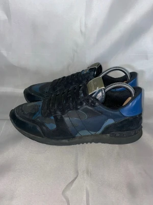 Valentino blå camo Rockrunners - Snygga sneakers från Valentino i svart och blått med camomönster. Skorna har svarta skosnören, svart sula och detaljer i mocka och läder. Perfekta för dig som vill ha en unik och trendig look.