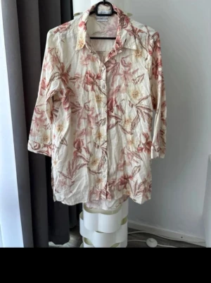 Blommig linneskjorta från Reserved - Snygg skjorta från Reserved i linnemix med blommigt mönster i beige och rödrosa toner. Skjortan har klassisk krage, knäppning framtill och trekvartsärm. Perfekt för dig som gillar en avslappnad och trendig stil.