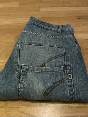 Blå dundup jeans (specialdesign) - Lite schysstare par blå jeans med raka ben och stora bakfickor med dekorativa sömmar. Jeansen har bälteshällor och klassisk femficksdesign. Specialdesignade med slitningar och dubbelfickor baktill (den övre fickan är bara design och ingen riktig ficka)