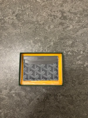 Grå kortfodral  - Snyggt grått kortfodral med det klassiska vita mönstret och logotypen tryckt på framsidan. Tillverkat i tåligt canvasmaterial med detaljer i läder. Perfekt för kort och sedlar, smidig att ha i fickan eller väskan.